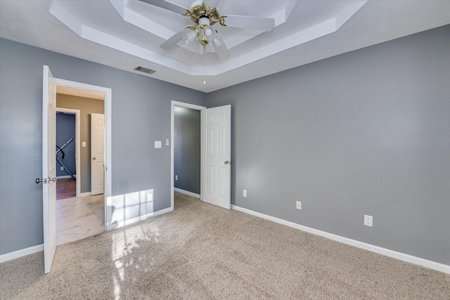 unfurnished bedroom featuring ceiling fan, light colored carpet, and a tray ceiling