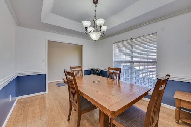 dining area featuring a raised ceiling, crown molding, a notable chandelier, and light hardwood / wood-style flooring