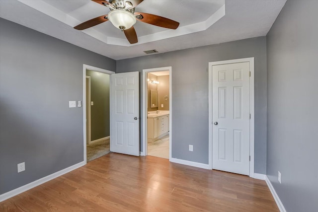 unfurnished bedroom with ceiling fan, connected bathroom, light hardwood / wood-style floors, and a tray ceiling