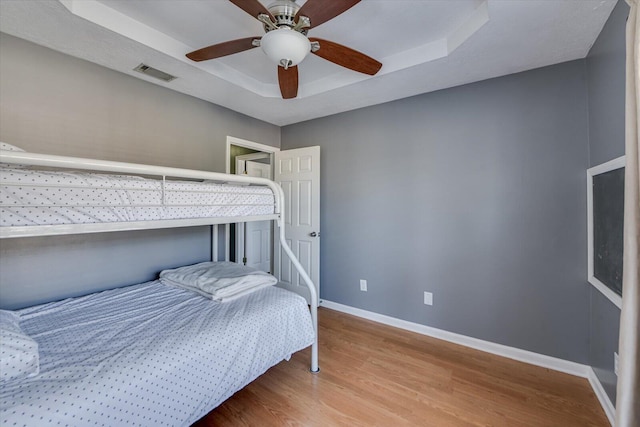 bedroom featuring hardwood / wood-style floors, a raised ceiling, and ceiling fan