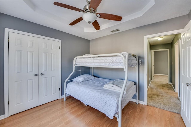 bedroom featuring ceiling fan, a tray ceiling, light hardwood / wood-style floors, and a closet