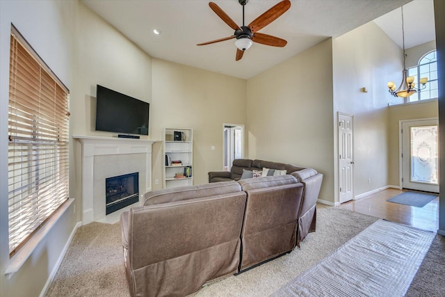 living room with a tiled fireplace, hardwood / wood-style floors, ceiling fan with notable chandelier, and a high ceiling