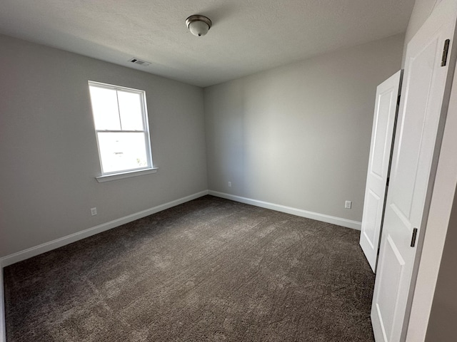 empty room with a textured ceiling and dark colored carpet