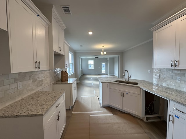 kitchen featuring sink, white cabinets, ornamental molding, kitchen peninsula, and light stone countertops