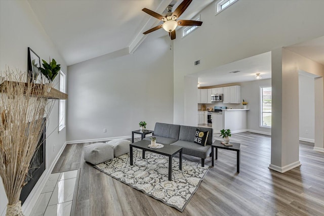 living room with visible vents, baseboards, high vaulted ceiling, light wood-style flooring, and a fireplace