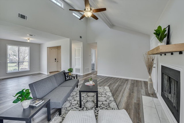 living room featuring a ceiling fan, wood finished floors, visible vents, baseboards, and a fireplace with flush hearth