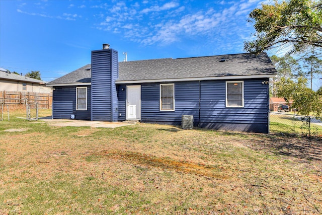 rear view of house featuring a lawn, central AC, fence, roof with shingles, and a chimney