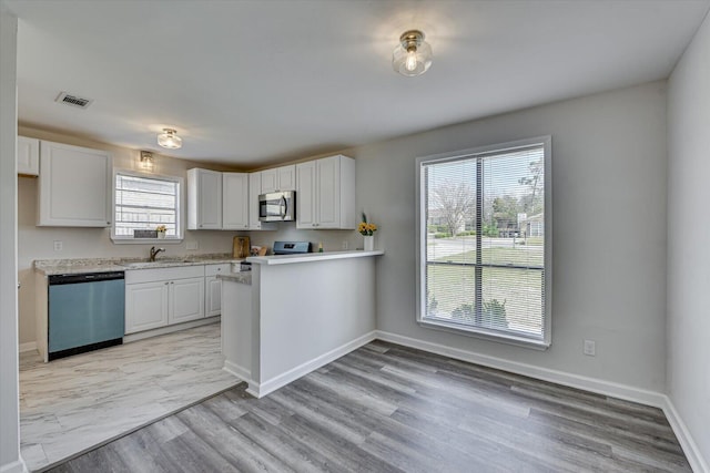 kitchen featuring a sink, stainless steel appliances, white cabinets, light countertops, and baseboards