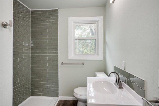 bathroom with hardwood / wood-style floors, toilet, a tile shower, and vanity