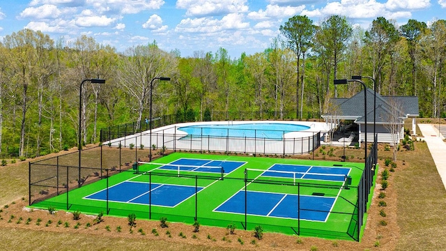 view of basketball court featuring a community pool, a forest view, a tennis court, and fence