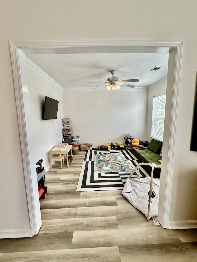 rec room featuring a textured ceiling, wood-type flooring, ornamental molding, and ceiling fan