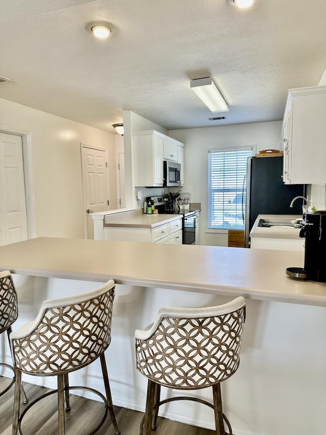 kitchen with white cabinetry, a breakfast bar area, kitchen peninsula, and appliances with stainless steel finishes