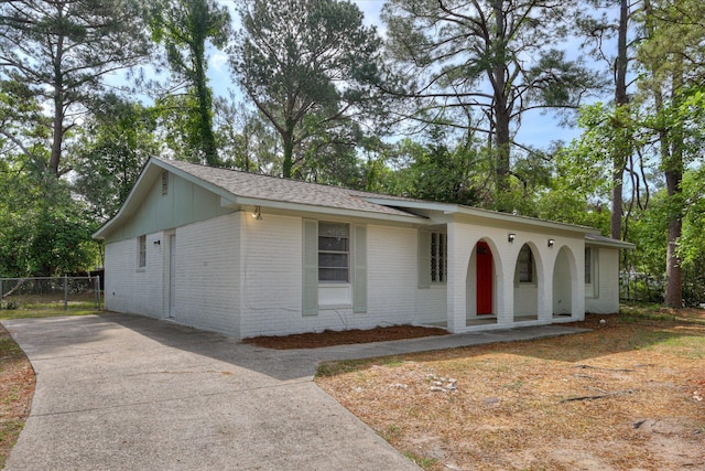 ranch-style home featuring a porch, concrete driveway, fence, and brick siding