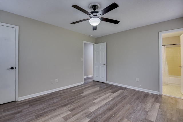 unfurnished bedroom with a ceiling fan, baseboards, wood finished floors, and ensuite bath