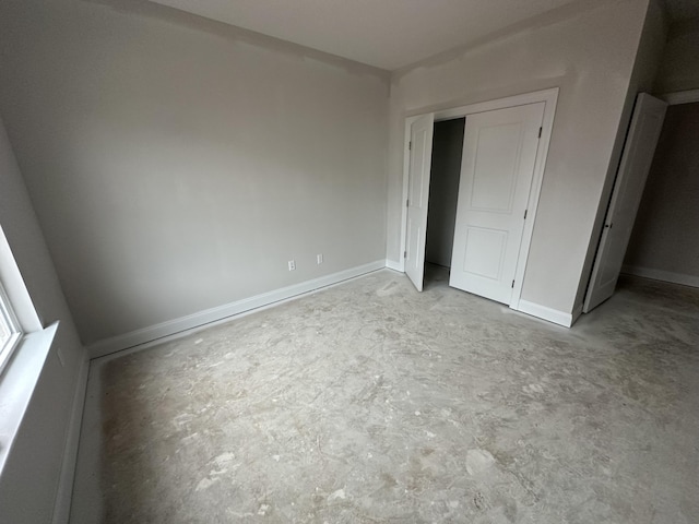 unfurnished bedroom featuring a closet, concrete floors, and baseboards