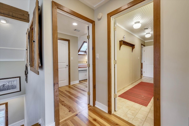 corridor featuring light wood finished floors, visible vents, crown molding, and baseboards