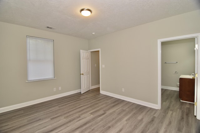 unfurnished bedroom with hardwood / wood-style flooring, sink, a walk in closet, and a textured ceiling