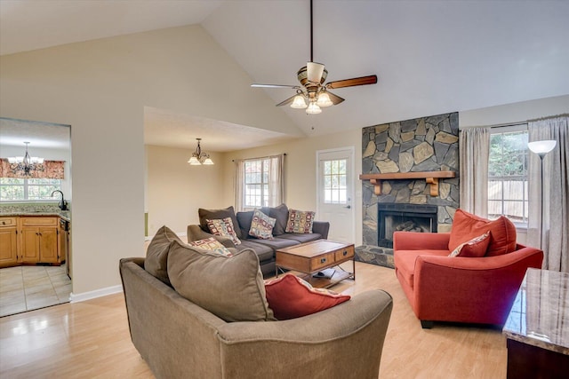 living room featuring sink, high vaulted ceiling, light hardwood / wood-style floors, a fireplace, and ceiling fan with notable chandelier