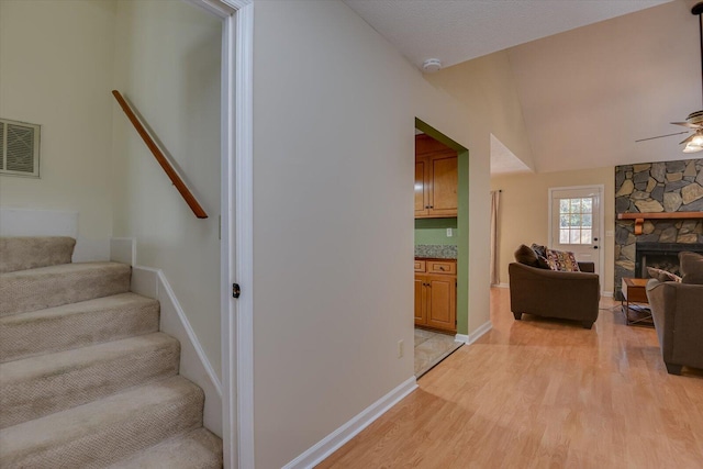 stairway with a fireplace, hardwood / wood-style floors, ceiling fan, and lofted ceiling