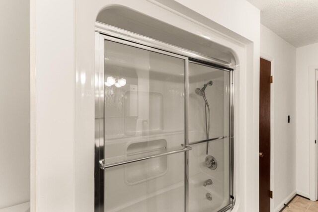 bathroom with a textured ceiling and bath / shower combo with glass door