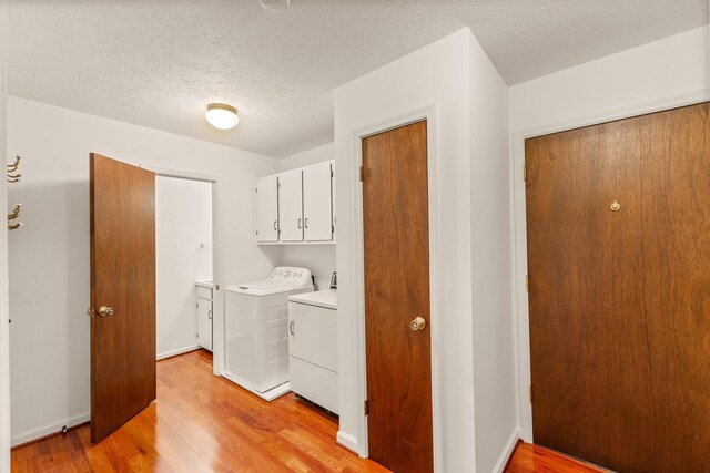 washroom featuring cabinets, a textured ceiling, light hardwood / wood-style floors, and washing machine and clothes dryer