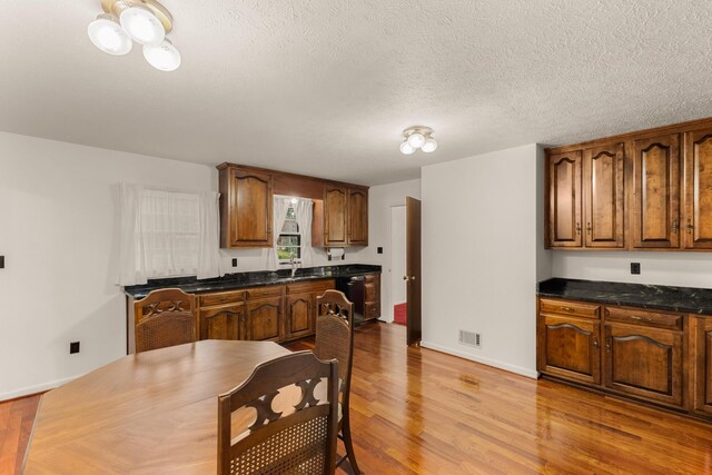 kitchen with dishwasher, a textured ceiling, light wood-type flooring, and sink