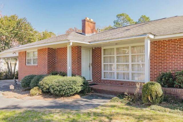 entrance to property with a shingled roof, brick siding, a chimney, and a carport