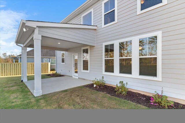 property entrance featuring fence, a lawn, and a patio