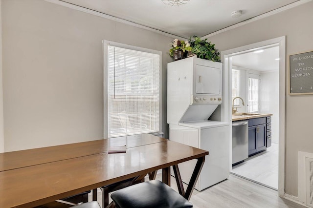 dining room with stacked washer and clothes dryer, sink, light wood-type flooring, ornamental molding, and a wealth of natural light