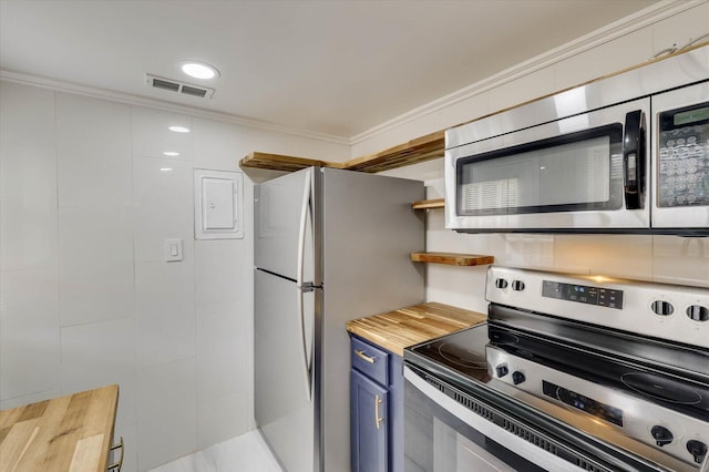 kitchen with appliances with stainless steel finishes, crown molding, blue cabinets, and butcher block counters