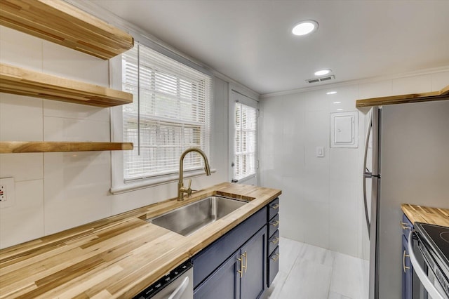 kitchen with blue cabinetry, stainless steel refrigerator, sink, wood counters, and stove