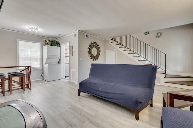 living room featuring light hardwood / wood-style floors, ornamental molding, and stacked washer / dryer