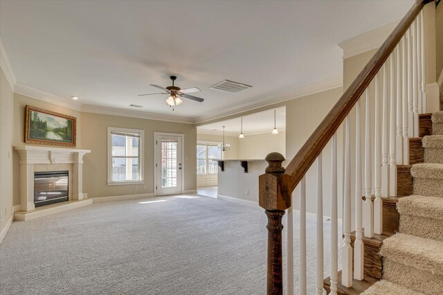 interior space with light carpet, a fireplace, crown molding, and ceiling fan