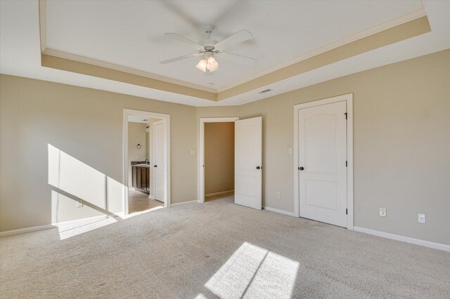 unfurnished bedroom featuring a raised ceiling, connected bathroom, ceiling fan, and light colored carpet