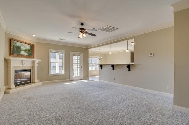 unfurnished living room with ceiling fan with notable chandelier, light colored carpet, crown molding, and a tiled fireplace