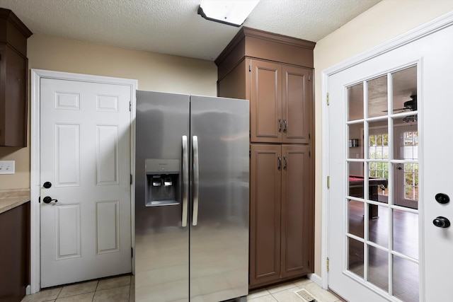 kitchen with stainless steel fridge with ice dispenser, a textured ceiling, light tile patterned floors, and dark brown cabinets