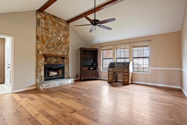 unfurnished living room featuring light wood-type flooring, lofted ceiling with beams, a stone fireplace, and ceiling fan