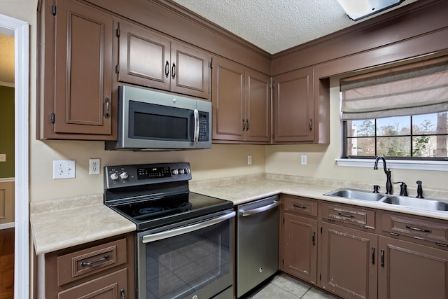 kitchen with a textured ceiling, light tile patterned floors, sink, and appliances with stainless steel finishes