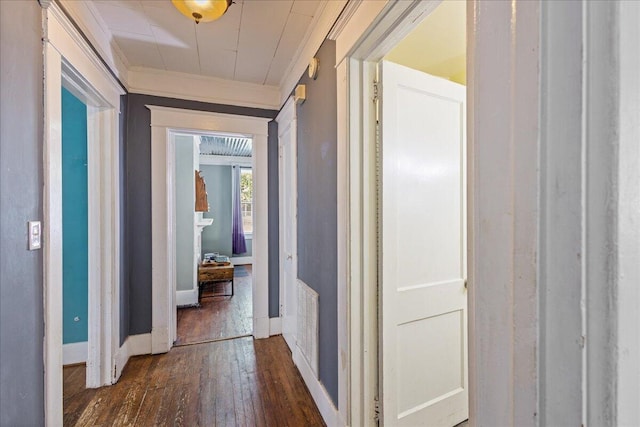 corridor featuring dark wood-type flooring, crown molding, and baseboards