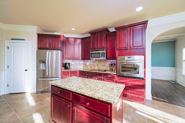 kitchen featuring ornamental molding, light tile patterned floors, light stone countertops, a kitchen island, and appliances with stainless steel finishes