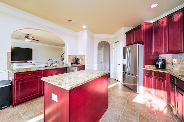 kitchen featuring stainless steel appliances, light stone countertops, ceiling fan, a kitchen island, and sink