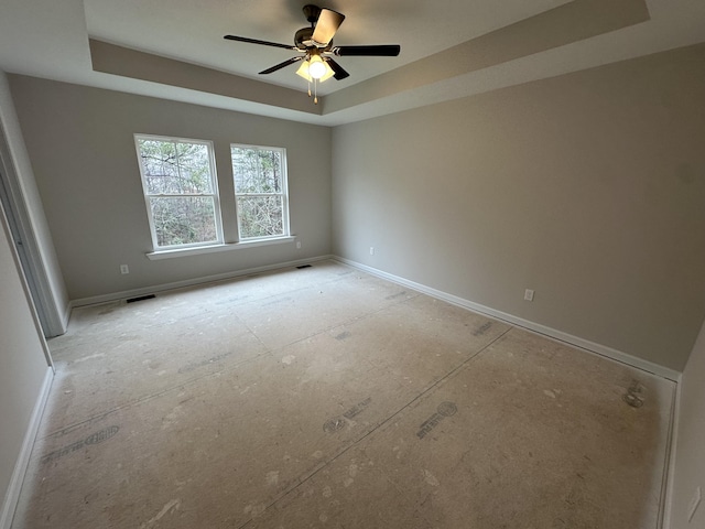 spare room with a tray ceiling, baseboards, visible vents, and a ceiling fan