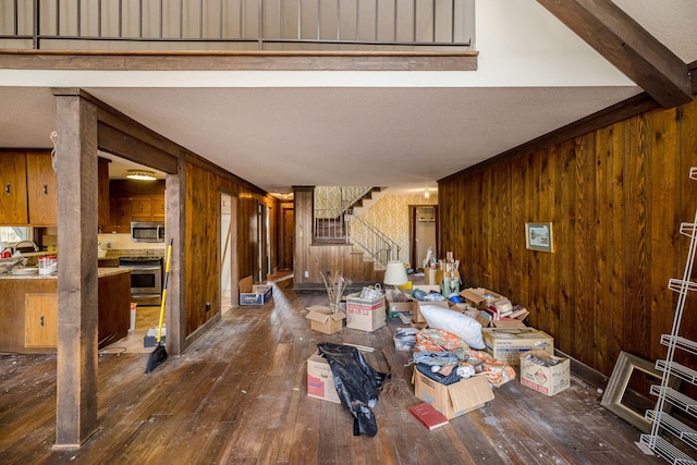 living room with wooden walls, dark wood-style floors, stairway, a textured ceiling, and beam ceiling