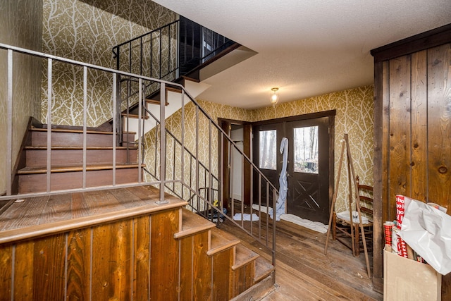 entryway with a textured ceiling, stairway, wood finished floors, and wallpapered walls