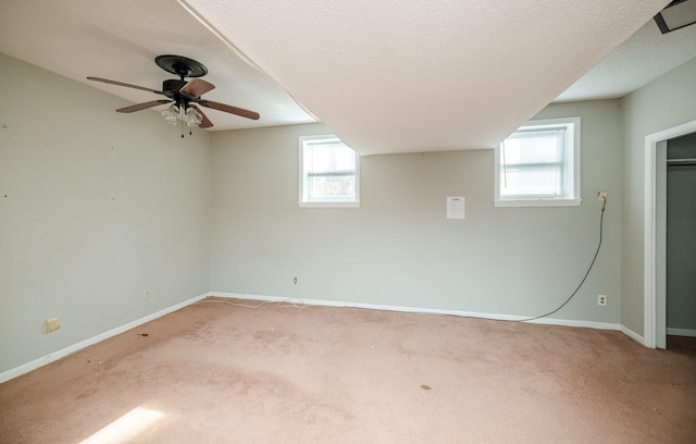 below grade area with a textured ceiling, ceiling fan, light carpet, and baseboards