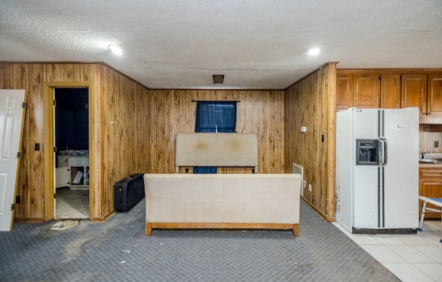 interior space with white refrigerator with ice dispenser, brown cabinetry, light colored carpet, a textured ceiling, and wood walls