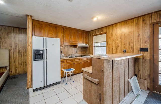 kitchen with brown cabinets, under cabinet range hood, white fridge with ice dispenser, and light countertops