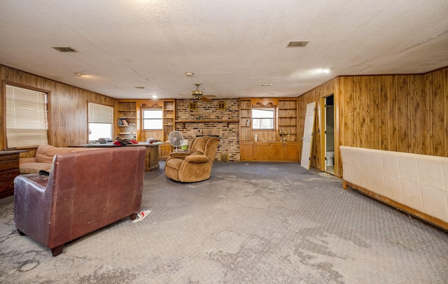 carpeted living area with wooden walls, visible vents, a fireplace, and a ceiling fan