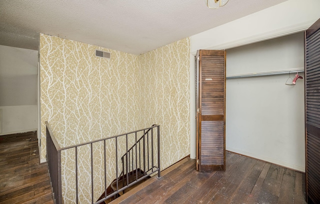 unfurnished bedroom with wallpapered walls, a textured ceiling, visible vents, and dark wood-type flooring