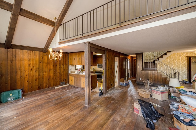 living room with dark wood-style flooring, an inviting chandelier, wood walls, beamed ceiling, and stairs